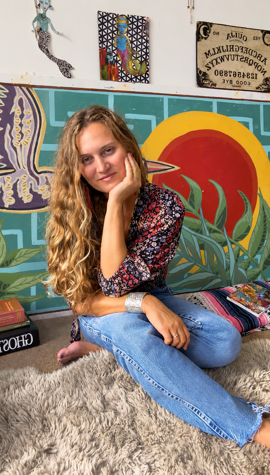 Kir sitting in front of her colorful hand-painted mural wall